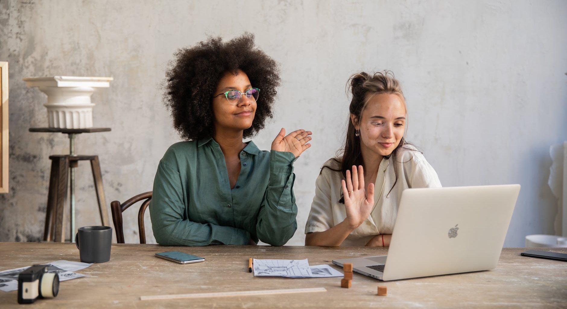 two women having their hands while looking at a laptop